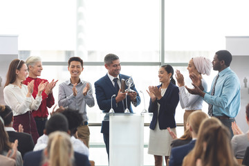 businessman holding award at podium with colleagues in a business seminar
