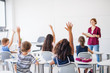 © Halfpoint - Rear view of school children sitting at the desk in classroom, raising hands.