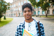 © Oleksandr - Smiling African American student with glasses and with books near college. Portrait of a happy black young man standing on a university background.