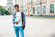 © Oleksandr - Smiling African American student with glasses and with books near college. Portrait of a happy black young man standing on a university background.