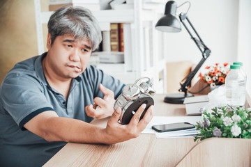 Wall Mural - Blurred of Asian man, He is patient from neurological diseases, or hemiplegia having a facial palsy and kinking fingers, He is looking at the alarm clock in his hand, to health and paralysis concept.