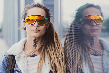 Wall Mural - Beautiful styilish girl in big toned glasses, tattoo on the neck and piercing is posing near mirroed wall.