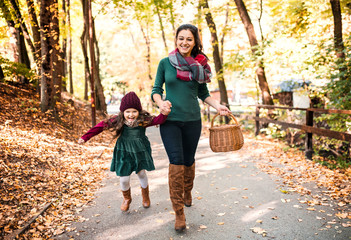 A young mother with a toddler daughter running in forest in autumn nature.