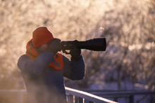 A Photographer With A Camera And A Telephoto Lens Shoots On A Frosty Winter Morning. Lebedinyj Swan Nature Reserve, Svetloye Lake, Urozhaynoye Village, Sovetsky District