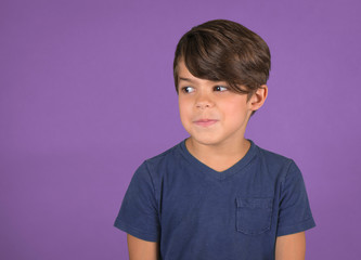 funny little boy looking to side with silly expression isolated on purple background