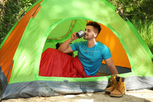 Young Man Drinking In Sleeping Bag Inside Tent