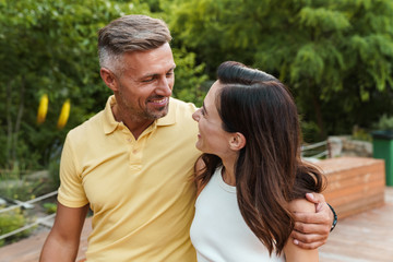 Wall Mural - Portrait of smiling middle-aged couple looking at each other and hugging while walking in summer park