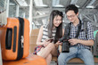 © Viewvie - Happy young asian couple waiting for the flight at the airport. They are sitting on the chair and look at the photo in a camera.