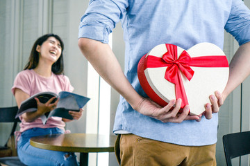 A boyfriend hiding a gift box behind his back surprising his girlfriend on special day.