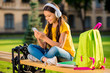 © deagreez - Portrait of her she nice attractive charming cute lovely cheerful cheery wavy-haired girl sitting on bench rest relax hobby using mp3 player in the street park town outside outdoors