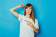 Young girl in a white T-shirt shows a finger on wet armpits from sweat on a blue background. Concept of excessive sweating, heat, deodorant