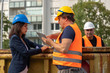 © cineberg - Construction manager wearing safety jacket and helmet checking projects discussing with a female engineer. In background, another worker