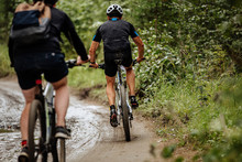 Back Two Cyclists Riding Mountain Bike On Dirty Trail In Forest