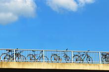Bicycles Parked At The Railing Of A Bridge In Front Of Blue Sky