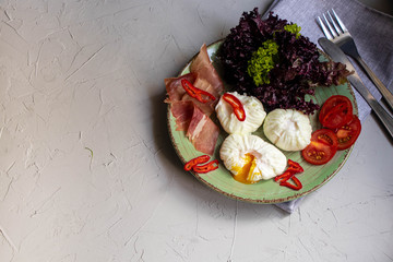 Poached egg - with slices of chili pepper, a sprig of dill, cherry tomatoes, Lettuce leaves and slices of bacon. For a healthy breakfast or snack. The plate lies on a gray napkin. Gray, stone backgrou