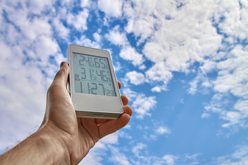 Wall Mural - Best personal weather station device with weather conditions inside and outside. A man holds a gadget in his hand on a background of sky and clouds