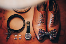 Stylish Watch, Expensive, Shoes, Bow Tie, Cufflinks And Belt For Groom On Wooden Table In Hotel Room. Morning Preparation Before Wedding Ceremony. Men Accessory For Luxury Event