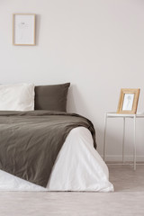  Graphic in wooden frame on white metal nightstand next to comfortable bed with black and grey pillows and duvet