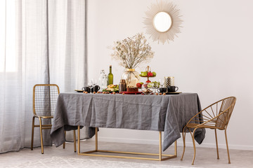 Trendy mirror in golden frame on white wall of elegant dining room