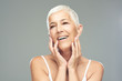 © chika_milan - Beautiful smiling senior woman with short gray hair posing in front of gray background. Beauty photography.