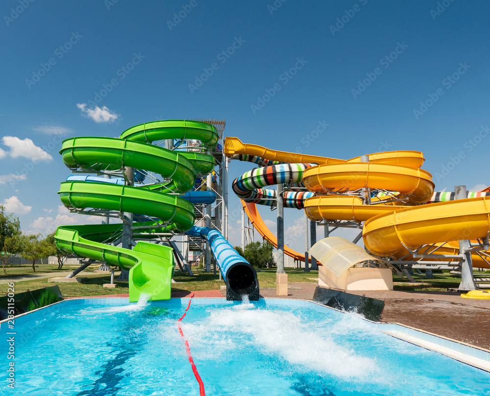 Water park, bright multi-colored slides with a pool. A water park without people on a summer day with a beautiful, cloudy blue sky - obrazy, fototapety, plakaty 