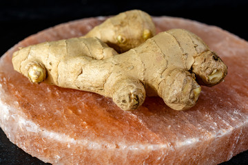 Fresh ginger roots on pink salt board close up on black wooden background