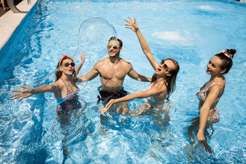 Wall Mural - Company of young merry girls and guy are having fun with huge soap bubbles in the swimming pool on the open air on a sunny summer day