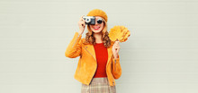 Happy Smiling Woman With Autumn Yellow Maple Leaves, Retro Camera Taking Picture In French Beret Over Gray Wall Background