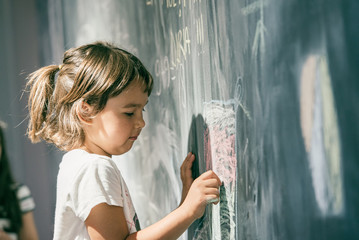 Beautiful little girl drawing on a blackboard at playground