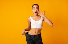 Excited Girl Posing In Oversize Jeans Over Yellow Studio Background