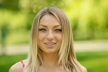 Wall Mural - Young smiling woman outdoors portrait. Soft sunny colors. Summer portrait of a beautiful young blonde outdoors in the city.