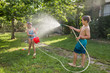 © Ramon Lopez/ADDICTIVE STOCK - Boy in swimwear splashing water from garden hose at a girl on a sunny day