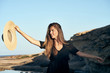 © Victor Bordera/ADDICTIVE STOCK - Young long haired smiling female model looking away holding hat in air on beach
