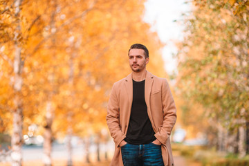 Young man drinking coffee with phone in autumn park outdoors