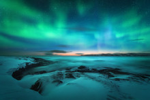 Aurora Borealis Over Rocky Beach And Ocean. Northern Lights In Teriberka, Russia. Starry Sky With Polar Lights. Night Winter Landscape With Aurora, Sea With Stones In Blurred Water, Snowy Mountains