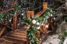Festive Christmas Decor Near The House. Street Decoration For Winter Holidays.Fir Branches With White Christmas Balls Ornate The Wooden Bridge In The Garden.Concept Happy Christmas, New Year.