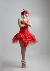 full length portrait of girl wearing red ballerina tutu and mask. dancing pose against a studio background.
