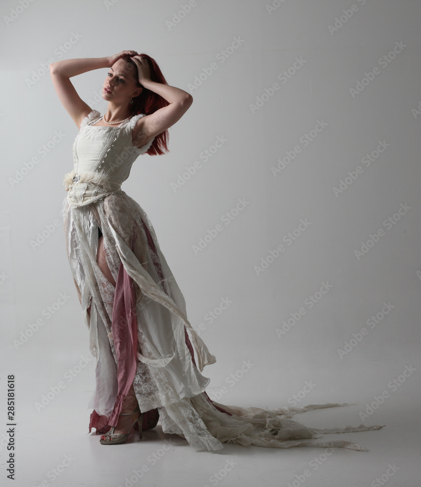 full length portrait of red haired girl wearing torn and tattered wedding  dress. Standing pose against a studio background with contrasty shadow  lighting. Stock Photo | Adobe Stock