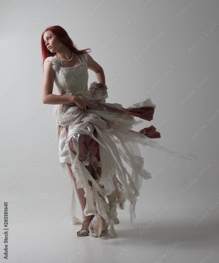 full length portrait of red haired girl wearing torn and tattered wedding  dress. Standing pose against a studio background with contrasty shadow  lighting. Stock-foto | Adobe Stock
