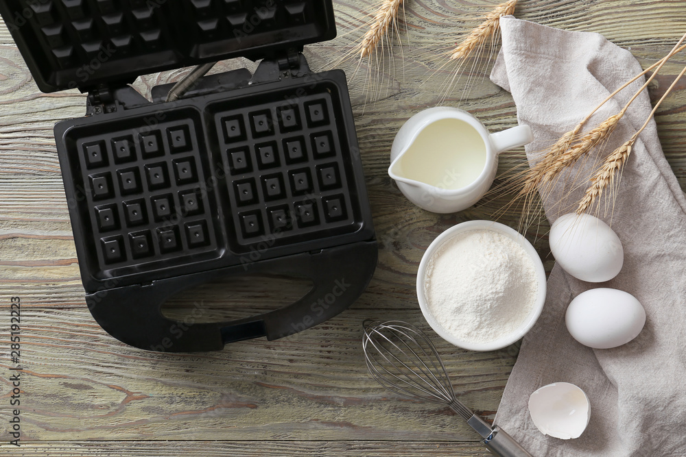 Modern waffle maker with ingredients on wooden table