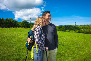 Young couple enjoying hiking together in nature standing on the top of the hill.