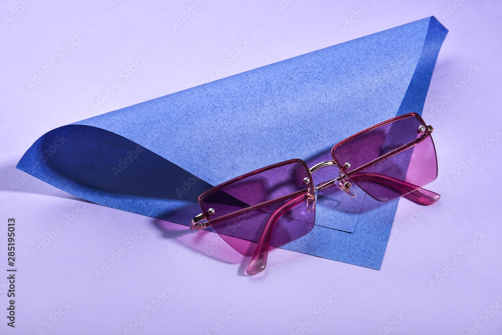 Stylish sunglasses and paper sheet on color background