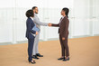 © Mangostar - Happy business colleagues welcoming each other in office corridor. Multiethnic business man and women standing in hallway and shaking hands. Handshake concept