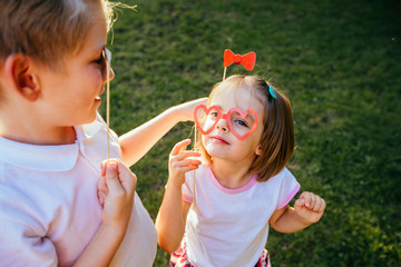 Funny kids playing together outdoors with paper accessories on a stick for a photo shoot on holiday or party in autumn park.