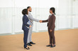 © Mangostar - Happy business partners meeting in office corridor. Multiethnic business man and women standing in hallway and shaking hands with each other. Business greeting concept