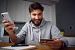 © baranq - Happy young man making payments from home online with smartphone and credit card