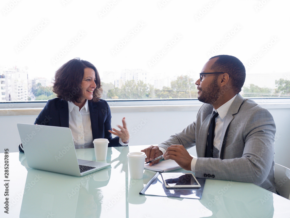 Happy female mentor explaining work issues to male intern. Business man and woman sitting at meeting table with open laptop and talking. Partnership concept - obrazy, fototapety, plakaty 