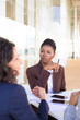 © Mangostar - Serious African American business woman discussing contract terms with partners in outdoor cafe. Multiethnic business colleagues sitting at table and talking. Business meeting outside concept