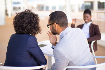 Male and female business colleagues whispering gossips about African American colleague. She laughing at them in background. Office conflict concept