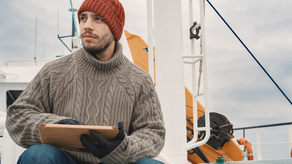 Dressed in Protective Coat Fisherman Using Tablet Computer with Navigation Maps while Traveling on Commercial Fishing Ship.
